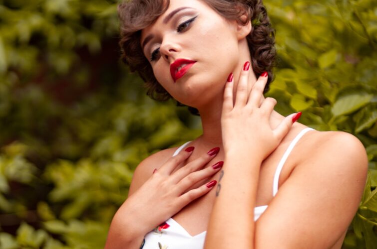 Model with classic red manicure and makeup poses in a garden setting, at Armani Nail Boutique, the best in the heart of Vancouver.