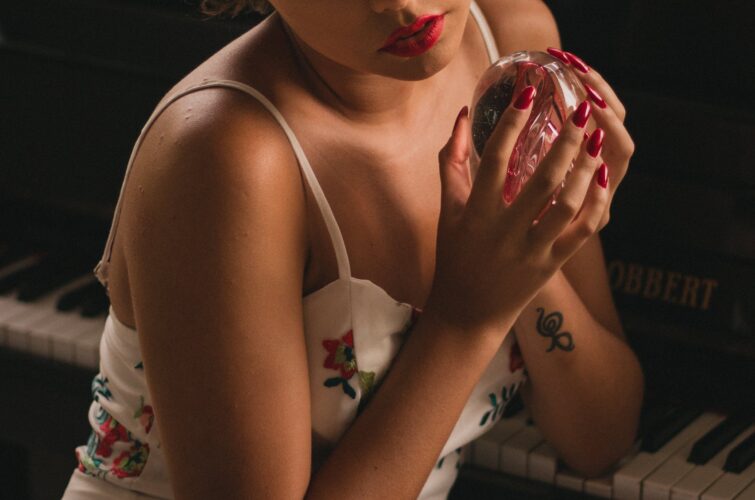Model with elegant red manicure holding a decorative glass object near a piano, at Armani Nail Boutique, the best in the heart of Vancouver.