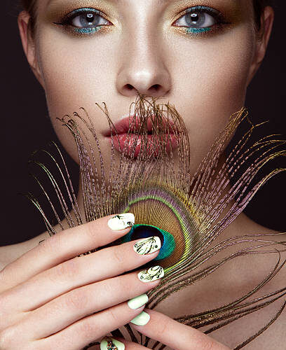 Model with intricate peacock-feather themed nail art and makeup, at Armani Nail Boutique, a premier North American salon.