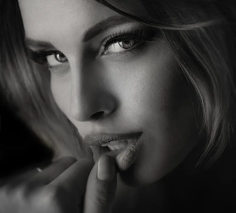 Alluring black and white close-up portrait of a person with defined eyes, long lashes and finger on their lips, featured on armaninail.com homepage.