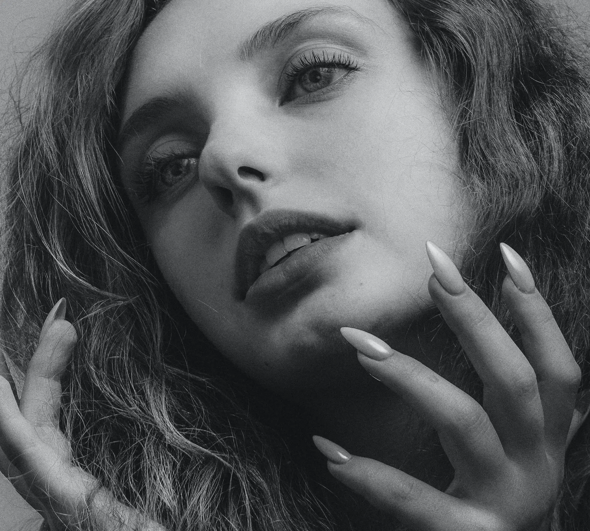 Black and white portrait featuring a person with expressive eyes, long eyelashes, and long, elegant nails, presented on armaninail.com