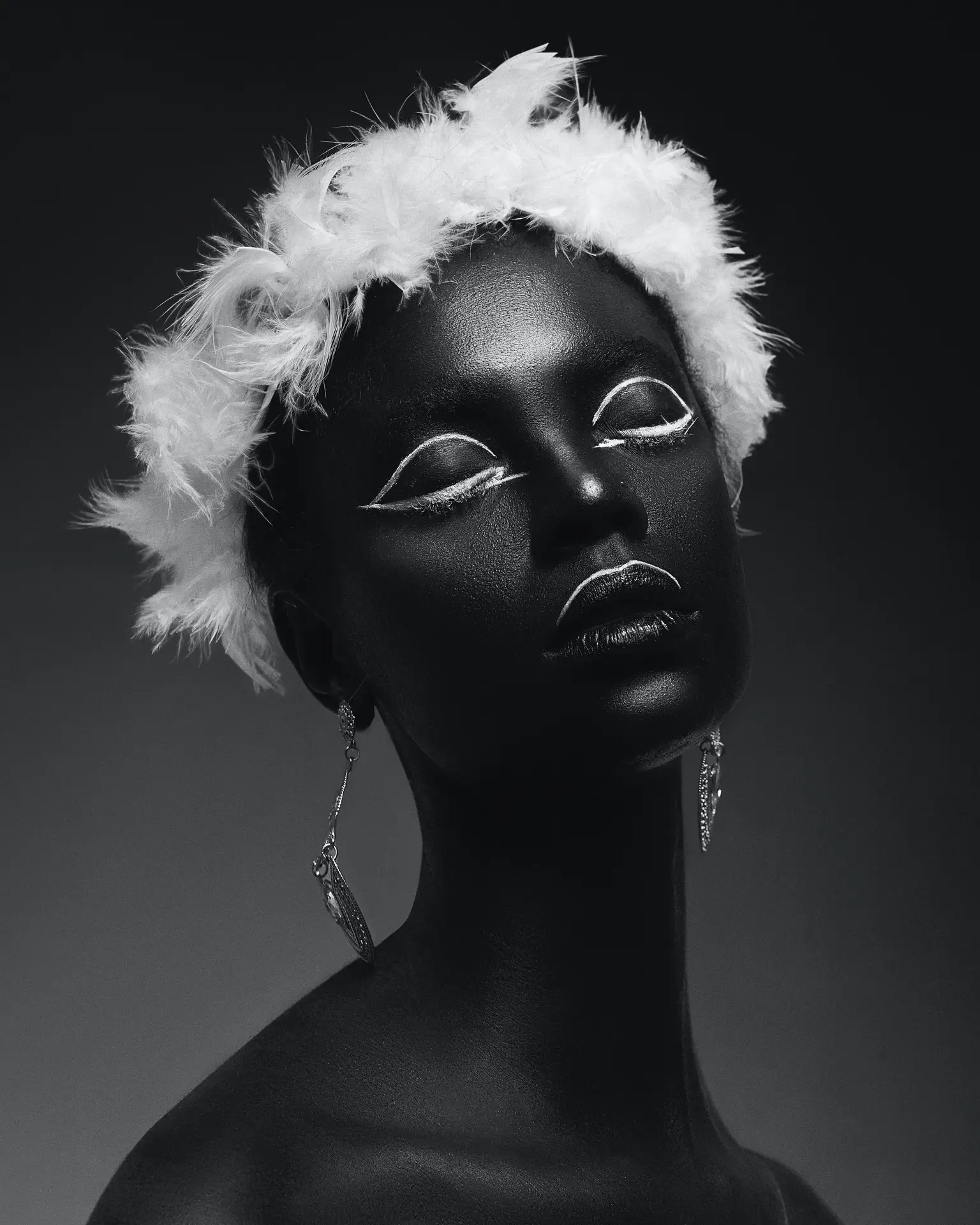 Artistic black and white portrait of a person with black body paint, white eyeliner, and a feather headdress, shown on armaninail.com.