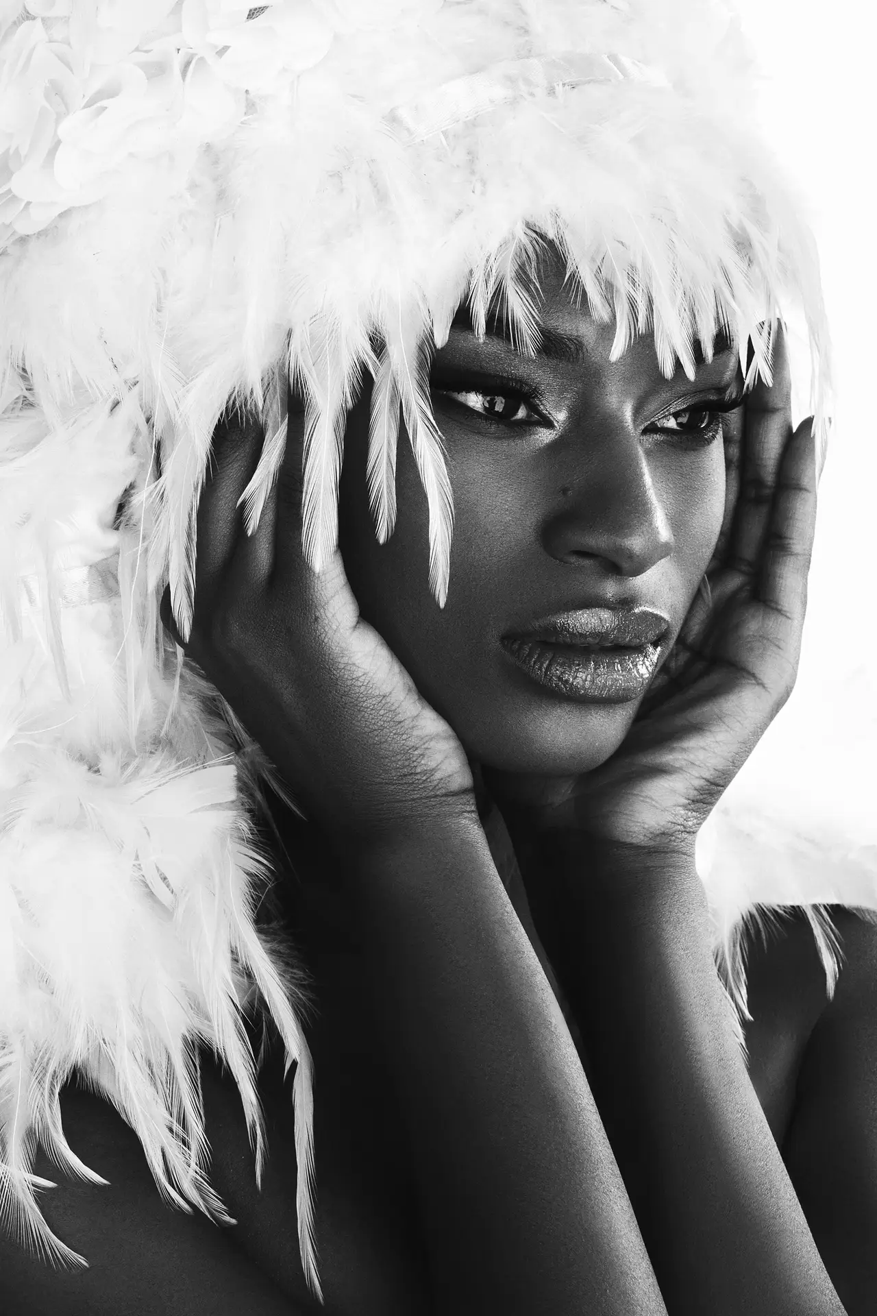 Black and white portrait of a person with expressive eyes, a feather headdress, and hands framing their face, as seen on armaninail.com
